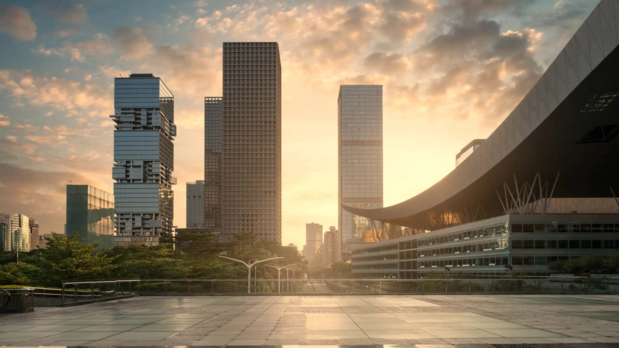 Corporate towers at sunset seen from a plaza, with a curved-roof building on the right