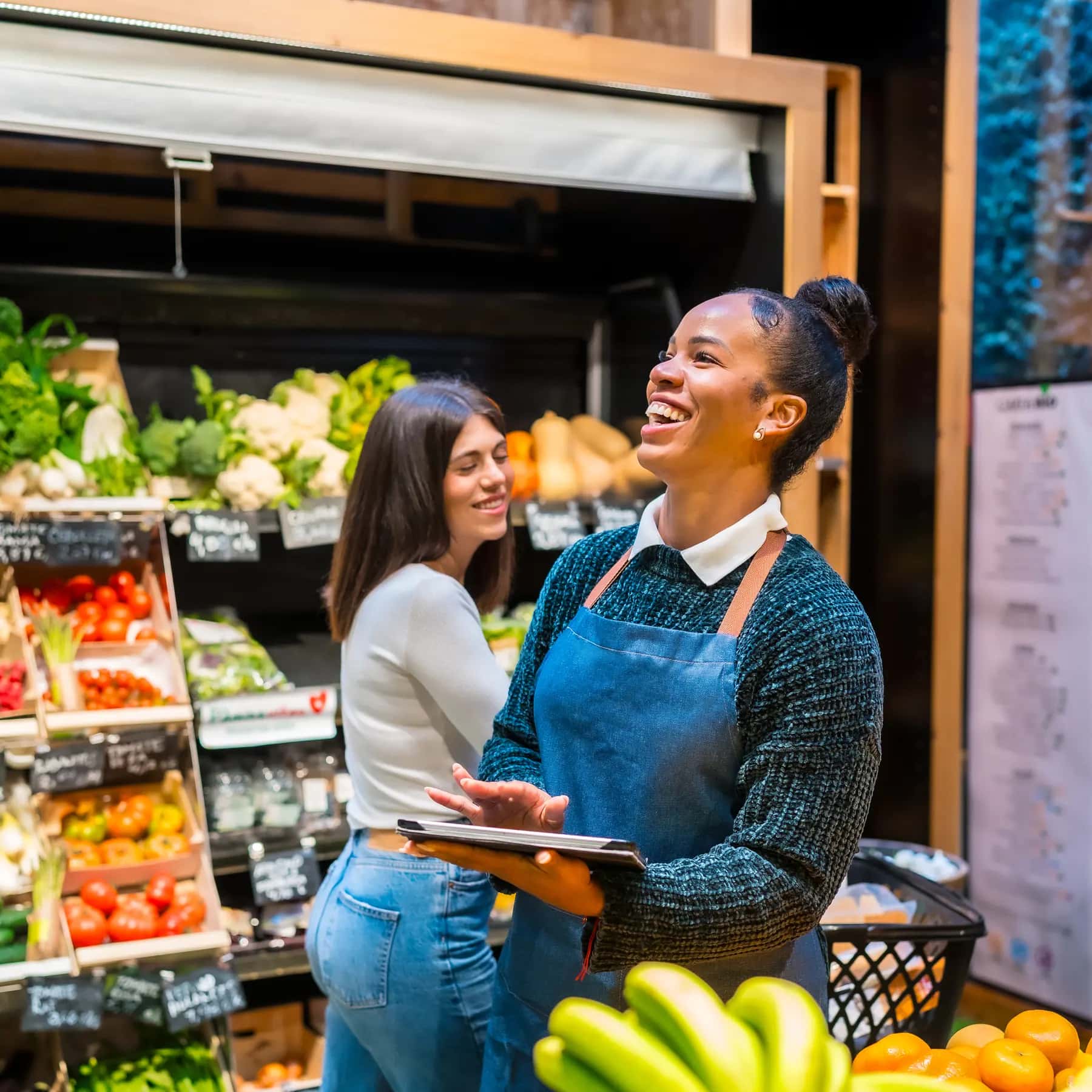 A store associate with a tablet helps a customer in the produce section