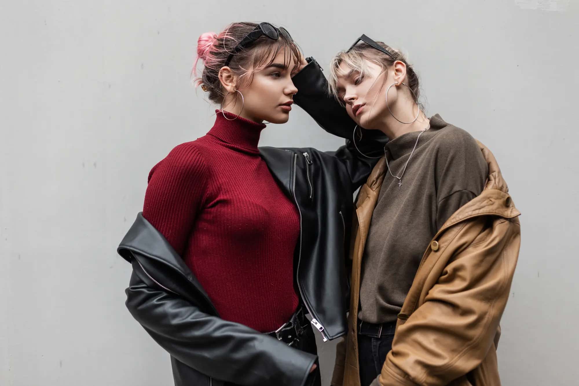 Two young women pose in winter coats against a gray wall